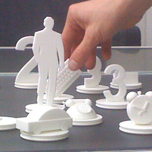 Weisse 3D gedruckte Figuren - Fiducials, das sind Bedien Objekte für einen Touchtable - Ziel Kundenberatung in einer Bank. Zu sehen sind Zahlen, ein reduziertes Auto, ein Telefon, ein Mann. Ausschnitt aus 30 Objekten.